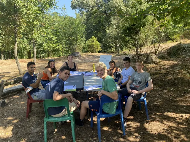 Des jeunes assis autour de deux tables, à l’ombre des arbres, pendant un atelier de français