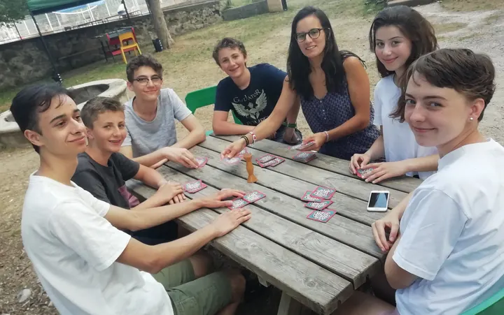 Des jeunes et une adulte souriants autour d’une table en bois, en pleine partie de cartes