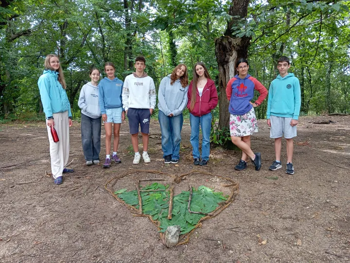 Huit jeunes debout dans la forêt derrière un grand cœur réalisé avec des feuilles, des branches et une corde