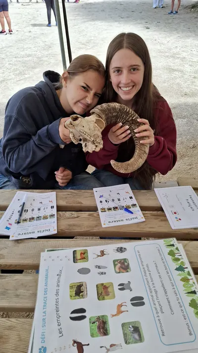 Deux participantes posant avec un crâne d’animal à grandes cornes, devant des fiches « Défis nature » posées sur une table