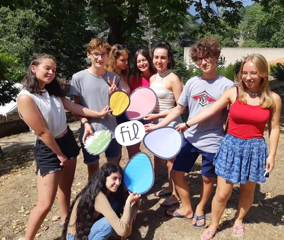 Huit jeunes en plein air qui tiennent ensemble de grands galets colorés autour du logo FIL