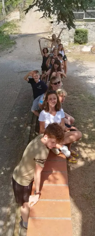 Jóvenes alineados a lo largo de un pequeño muro de ladrillo, en lo alto de un camino con sombra, vistos desde arriba