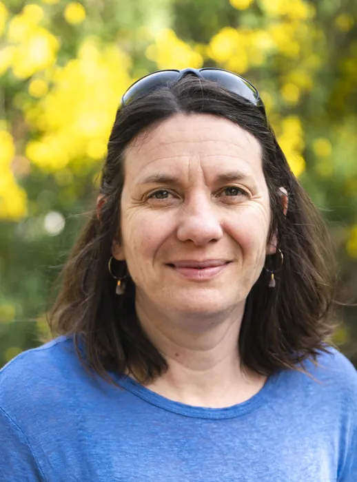 Portrait de Bénédicte, la directrice de FIL, souriante, devant un arbuste en fleurs jaunes