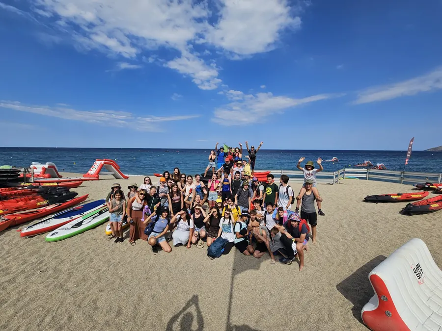 Un grand groupe de jeunes réunis sur la plage entre les kayaks et les paddles, au bord de la mer
