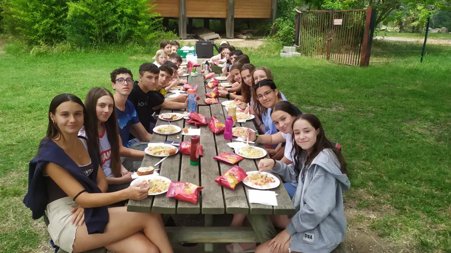 Des jeunes qui déjeunent ensemble à une longue table en bois, en plein air