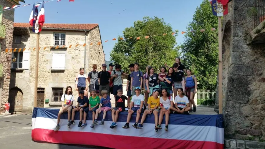 Alumnos sentados en una tarima engalanada de azul, blanco y rojo en una plaza del pueblo