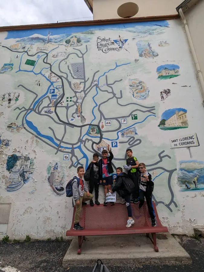 Cuatro alumnos posando delante de un gran mapa ilustrado pintado en una pared, durante un rally por el pueblo