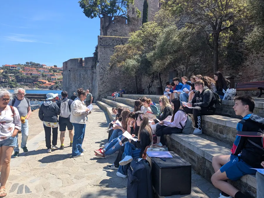 Un grupo de alumnos sentados en las gradas de piedra de Colliure con su guía, delante del castillo y del mar