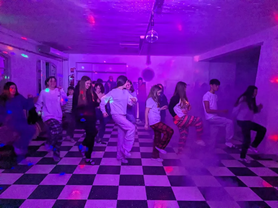 Alumnos bailando en una sala iluminada de morado, sobre un suelo de damero blanco y negro