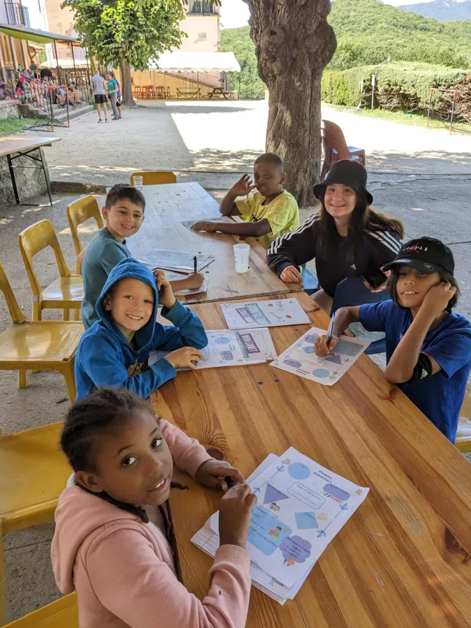 Young people posing around a wooden table during a workshop, exercise sheets in front of them