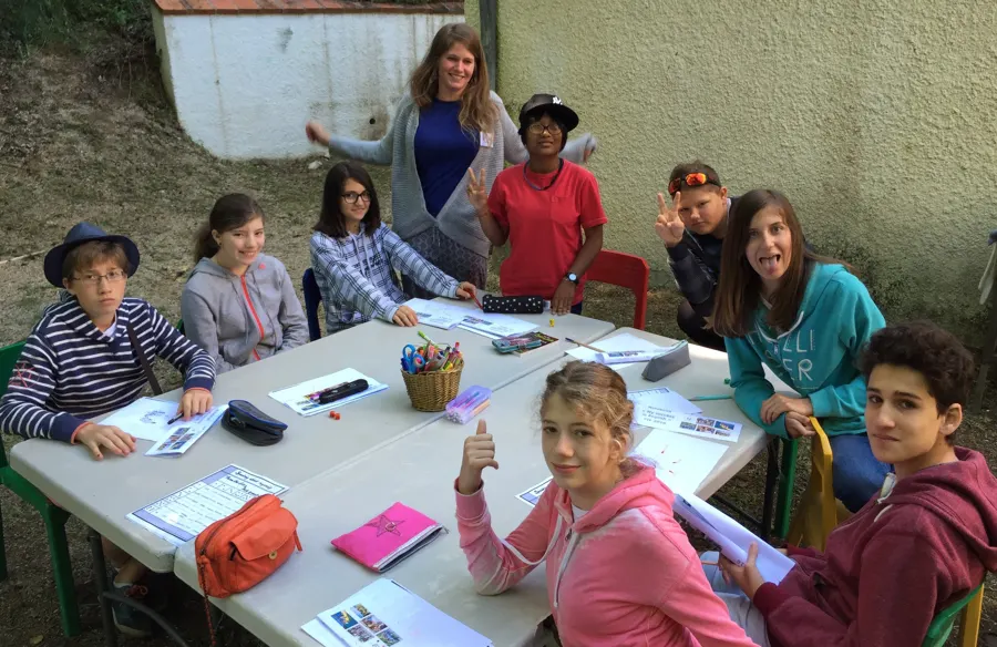 Young people and a team leader around a table, with notebooks and pencils, during an outdoor workshop
