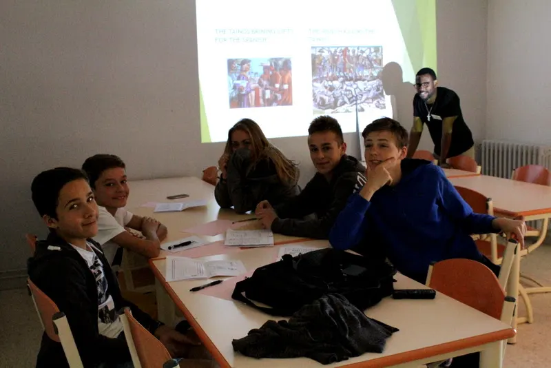 Young people sitting around a classroom table in front of a projection screen, during a workshop