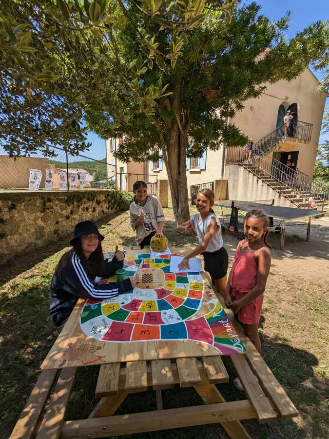 Young people playing a big colourful board game on a picnic table, in the courtyard of the estate