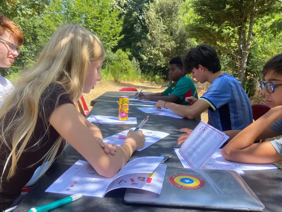 Young people working on sheets laid out on a big table, in the shade of the trees