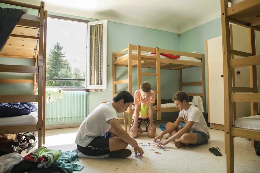 Trois garçons qui jouent aux cartes par terre dans une chambre du Noell, entre des lits superposés