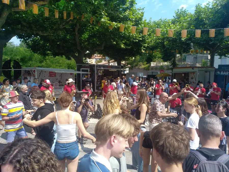 Des jeunes de FIL qui dansent sur la place du village pendant une fête, avec une fanfare et des drapeaux catalans