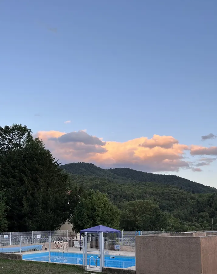 La piscine clôturée du Noell, au pied d’une colline boisée, sous un ciel de fin de journée