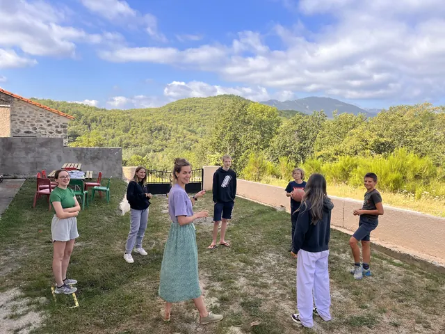 Des jeunes et une adulte debout en cercle sur une pelouse, devant des collines boisées