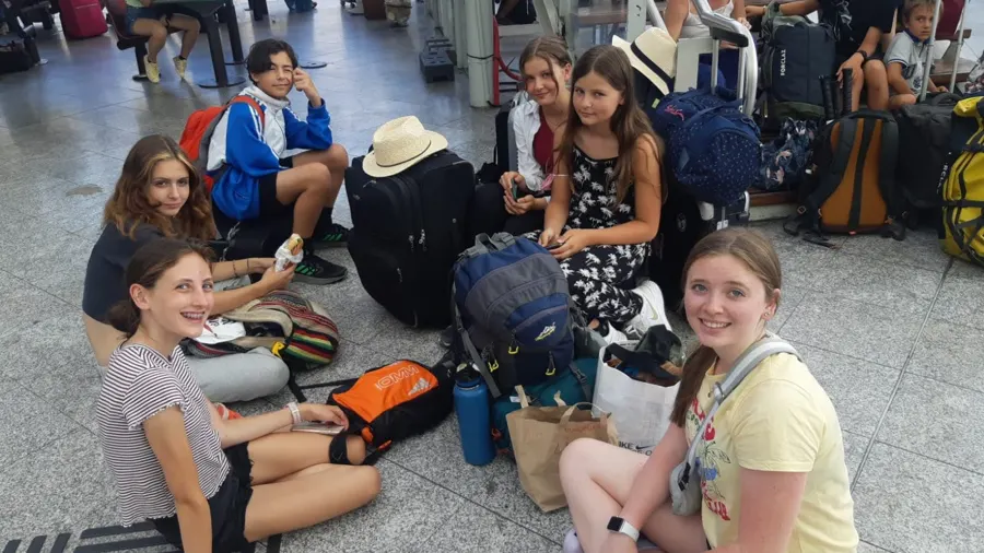 Cinq jeunes assis par terre avec leurs valises dans le hall de l’aéroport, en attendant leur navette