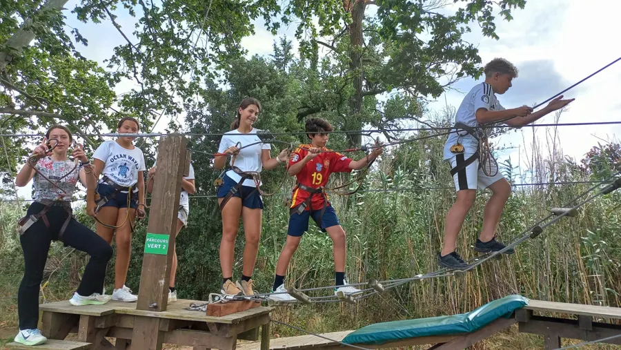 Fünf Jugendliche mit Klettergurt auf einer Holzbrücke in einem Hochseilgarten