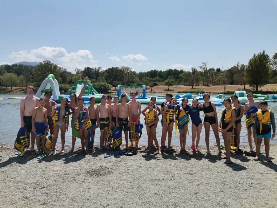 Eine große Gruppe Jugendlicher in Schwimmwesten am Seestrand, vor den aufblasbaren Aquajump-Konstruktionen