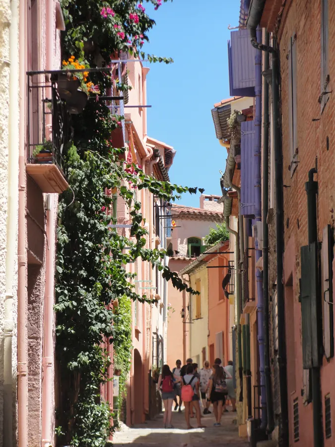 Eine bunte Gasse in Collioure, gesäumt von rosa Häusern und Blumen