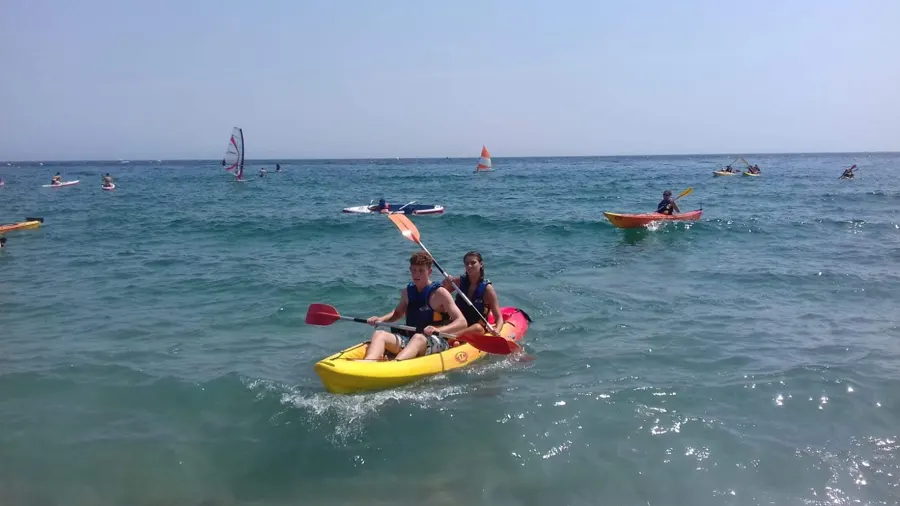 Zwei Jugendliche in einem gelben Kajak auf dem Mittelmeer, vor dem Strand
