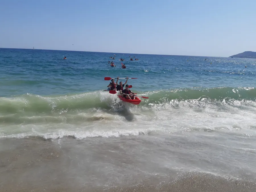 Ein Doppelkajak fährt am Strand über eine Welle