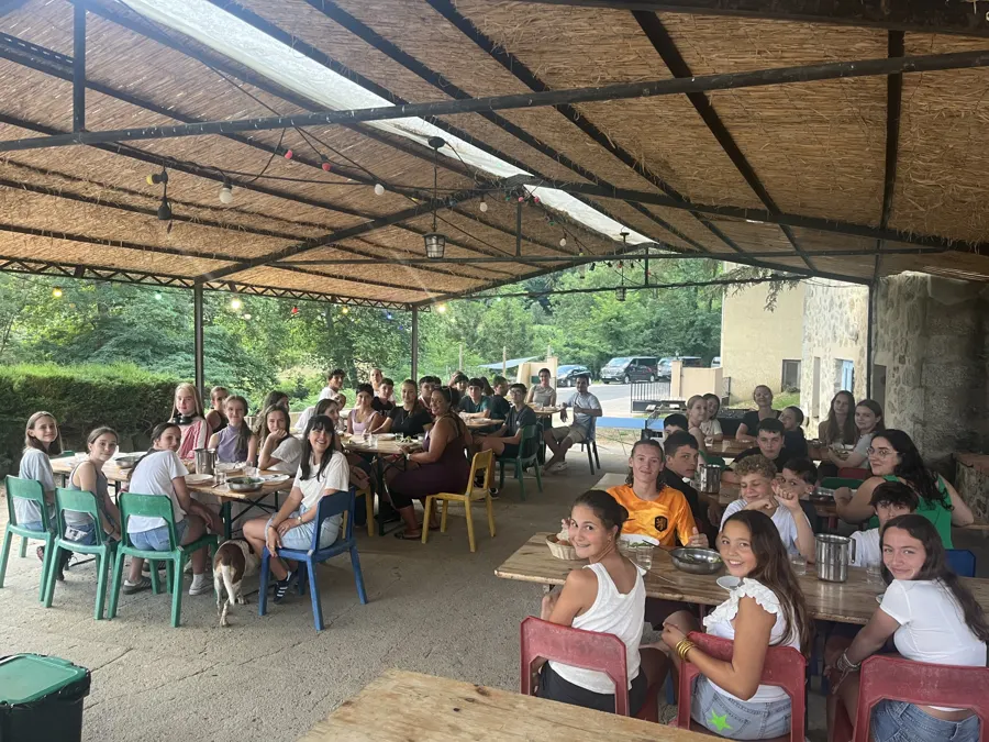 Eine große Gruppe Jugendlicher beim Mittagessen unter der überdachten Terrasse des Geländes