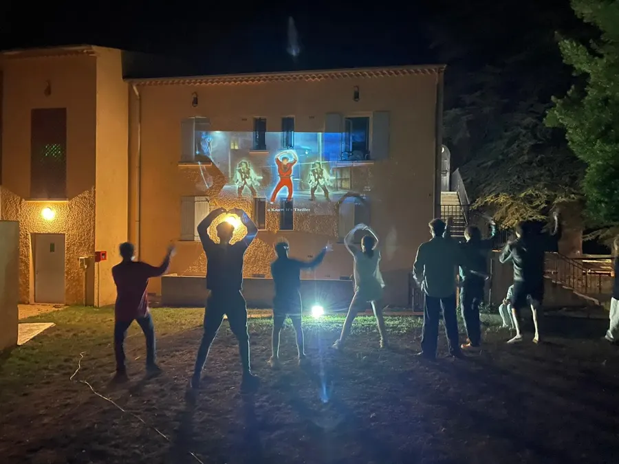 Jugendliche tanzen nachts im Garten, vor Bildern, die auf die Hauswand projiziert werden