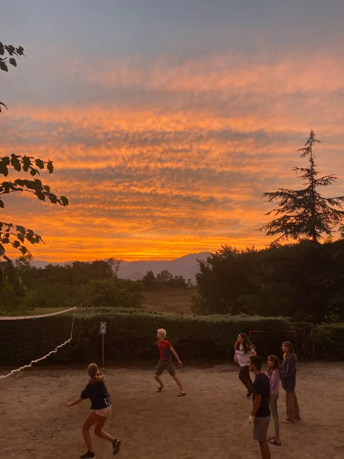 Jugendliche spielen Volleyball auf dem Sandplatz, unter einem orangefarbenen Sonnenuntergang