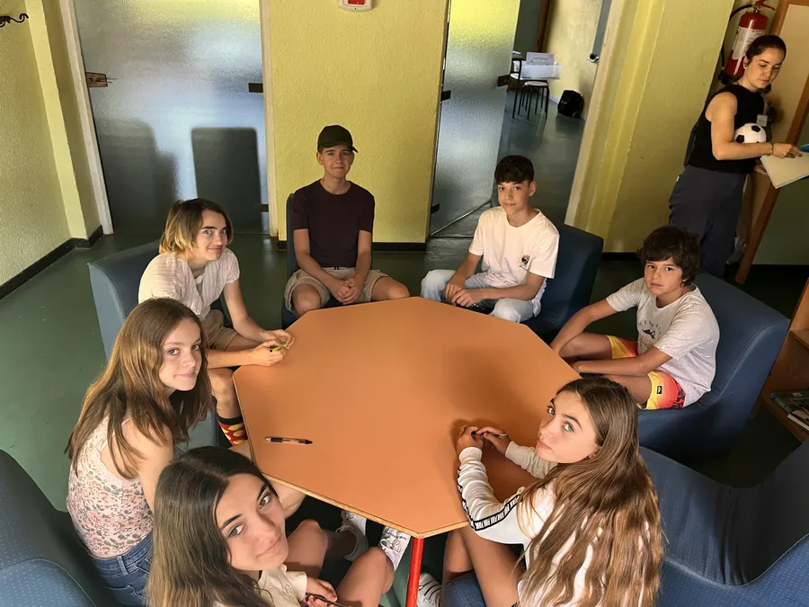 Des jeunes assis dans des fauteuils autour d’une table orange, en intérieur