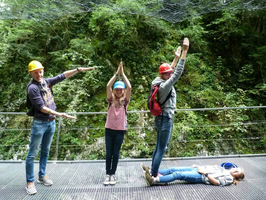 Sur une passerelle en forêt, trois personnes forment avec leur corps les lettres F, I et L, une quatrième est allongée au sol