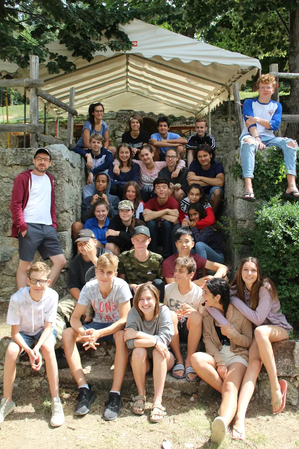 Un grand groupe de jeunes et d’animateurs assis sur les marches d’un muret en pierre, sous un barnum