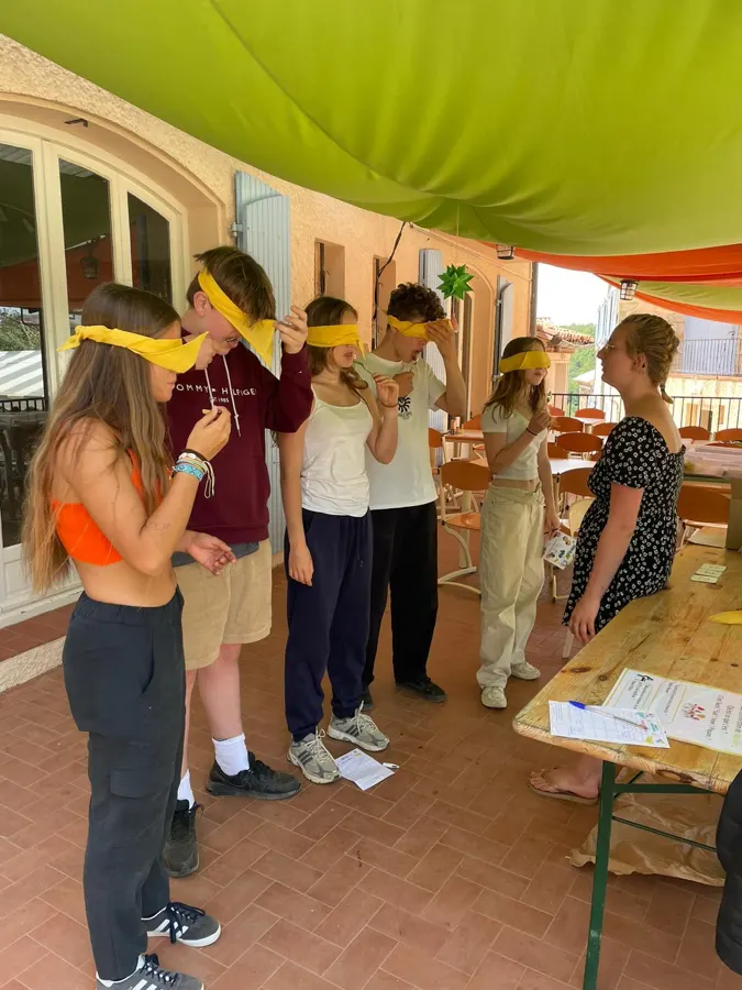 Des jeunes aux yeux bandés, debout autour d’une grande table sur la terrasse, pendant un jeu de dégustation