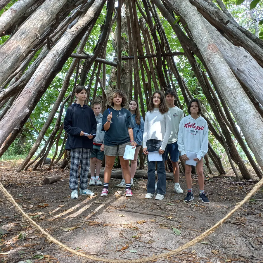 Un groupe de jeunes qui posent ensemble dans une grande cabane de branches, au milieu des bois