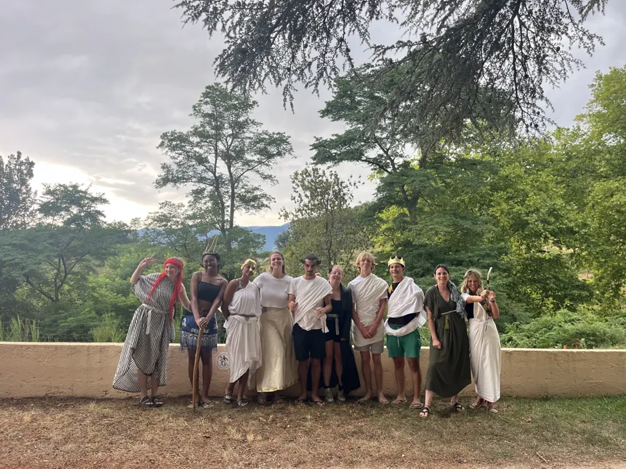 L’équipe d’animation en tenues de la Grèce antique, en toges blanches, qui pose sur un muret devant les arbres