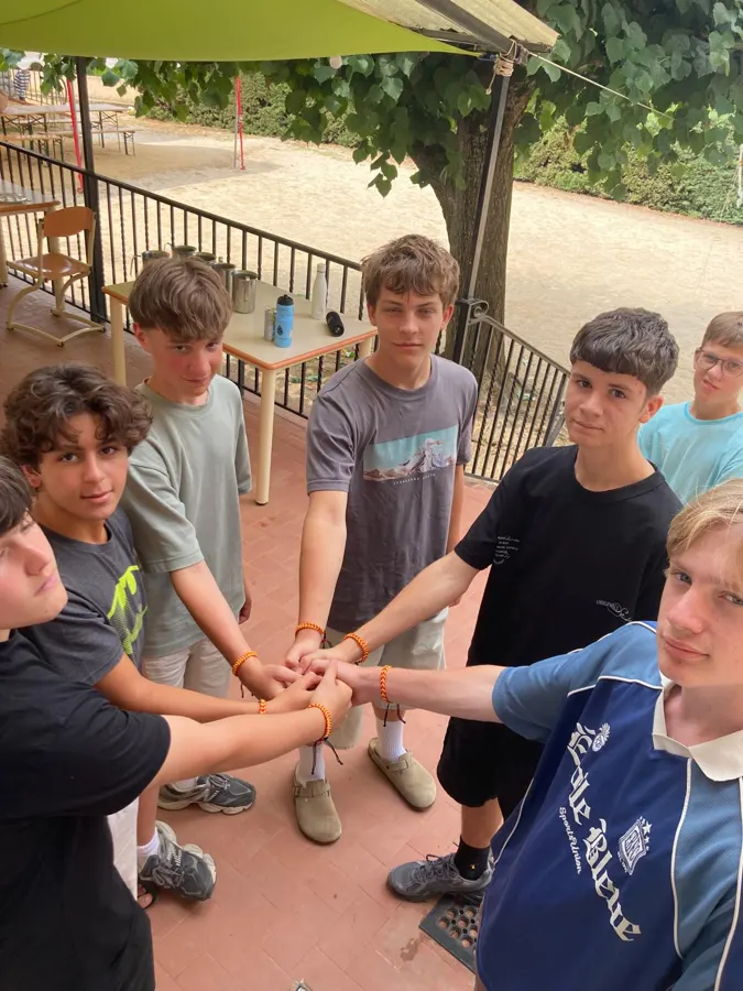 Des jeunes qui joignent leurs mains au centre du cercle, avec leurs bracelets, sur la terrasse
