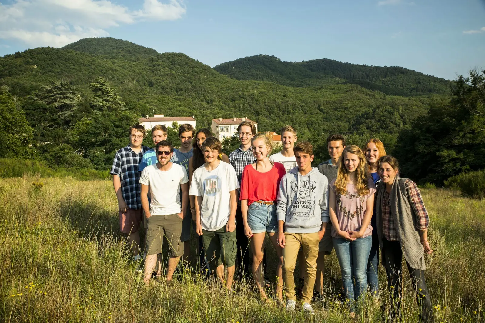 Une quinzaine de personnes posant ensemble dans une prairie, devant les montagnes boisées